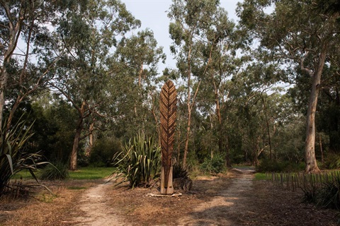 A photo of a wood carving at the middle of a forked path, surrounded by nature.