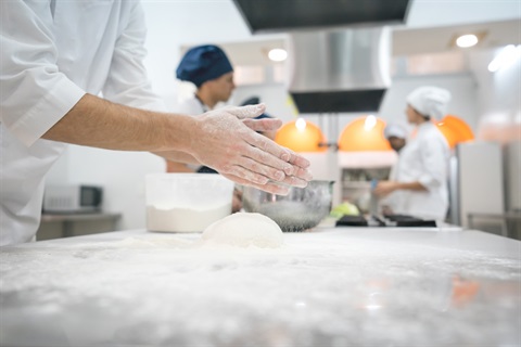 A person with flour on their hands prepares to knead dough in a professional kitchen.