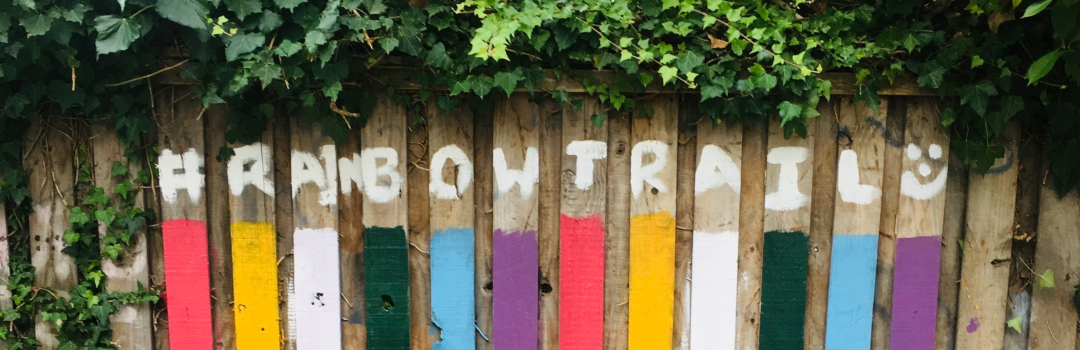 An image of a rainbow painted on a fence with the words 'rainbow trail'