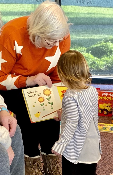 Women in orange jumper reading to children