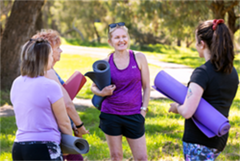 Group of women chatting while holding yoga mats in a park