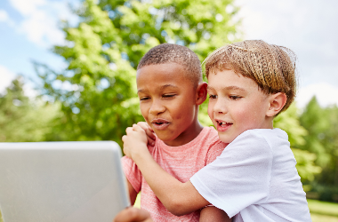 Two children sitting outside looking at a computer 